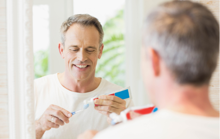 man in bathroom putting toothpaste on a toothbrush