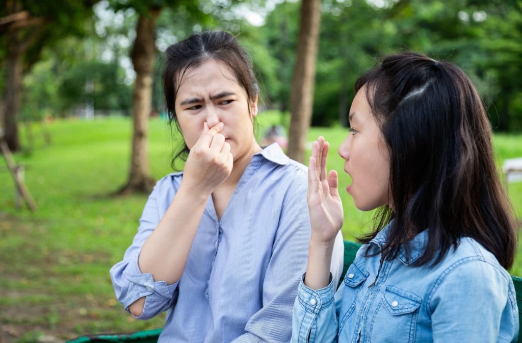 Woman plugging her nose as her friend with bad breath talks