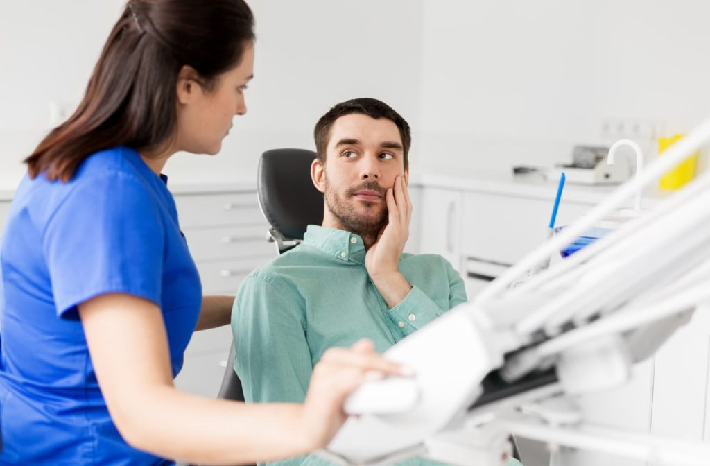 Dental patient holding his jaw and talking to his dentist about TMJ pain