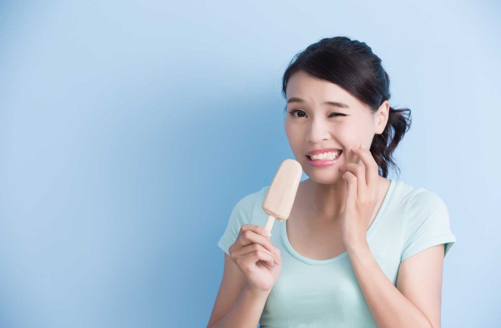 woman in a blue shirt holding ice cream touching face in pain from sensitive teeth