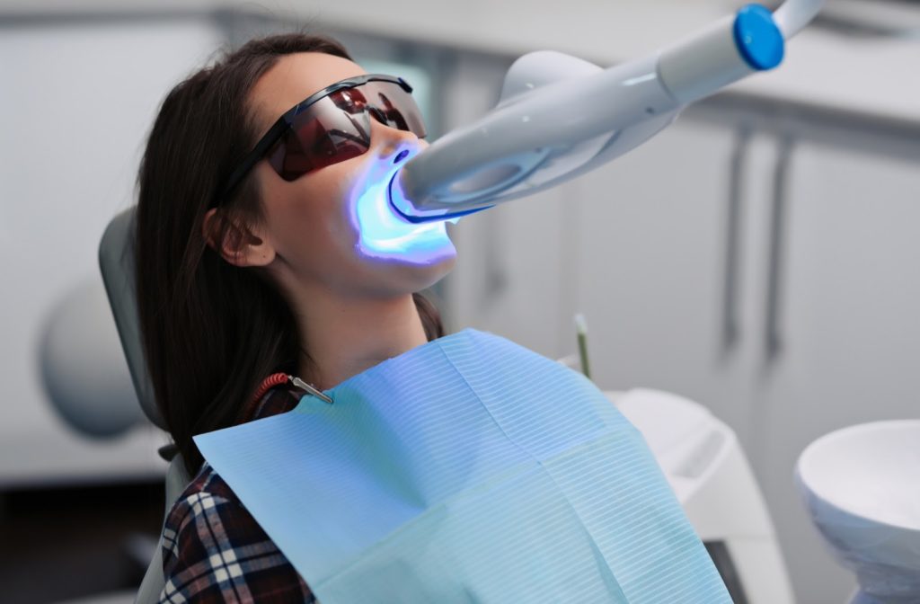 Woman in dentist's chair wearing protective glasses and getting a bleaching procedure activated by light