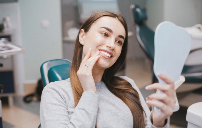 A woman sitting in a dentists chair looking at her newly whitened teeth