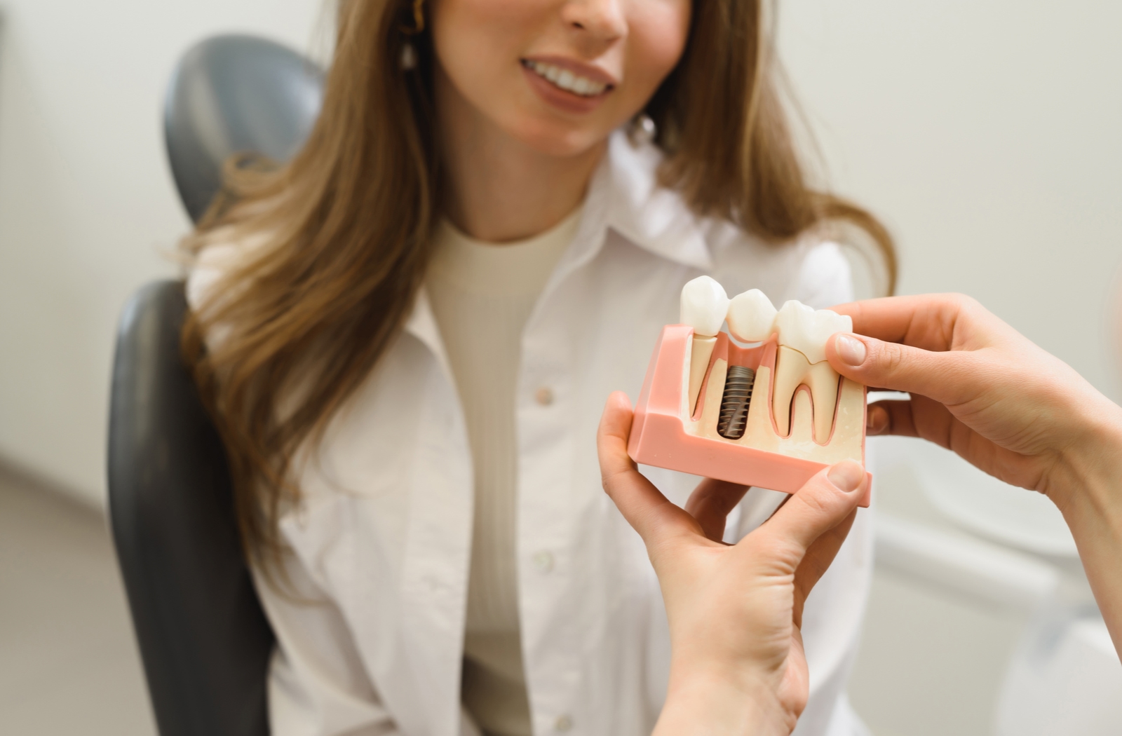 A dentist explaining to their female patient about dental implants while using a plastic model to simulate the procedure