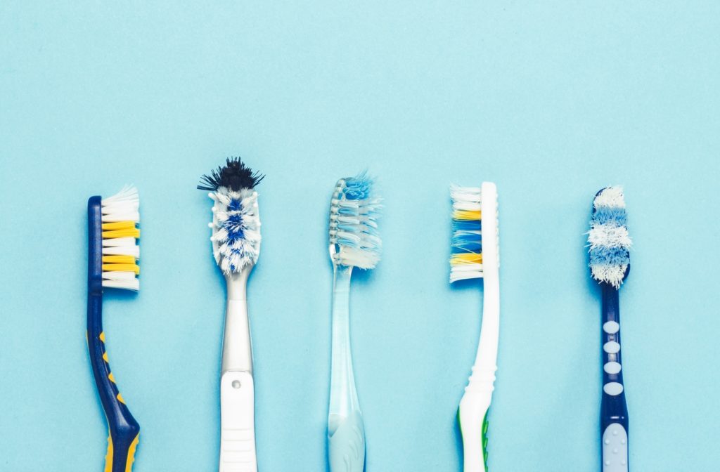 Five toothbrushes with different wear patterns all laying side by side on a light blue background
