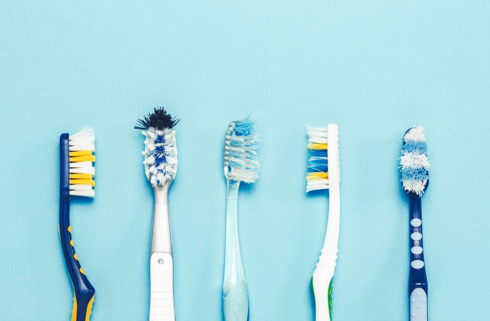 Five toothbrushes with different wear patterns all laying side by side on a light blue background