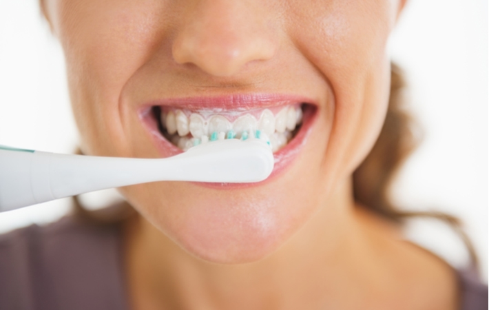 A close up of a woman's mouth, her teeth covered in toothpaste while shes brushing her teeth with a manual toothbrush
