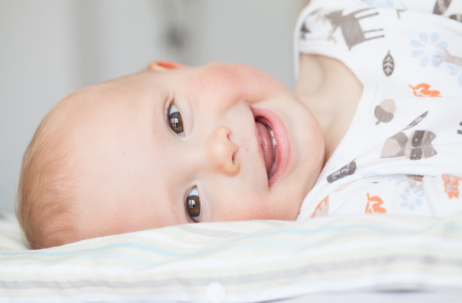 An image of a baby laying down, smiling at the camera