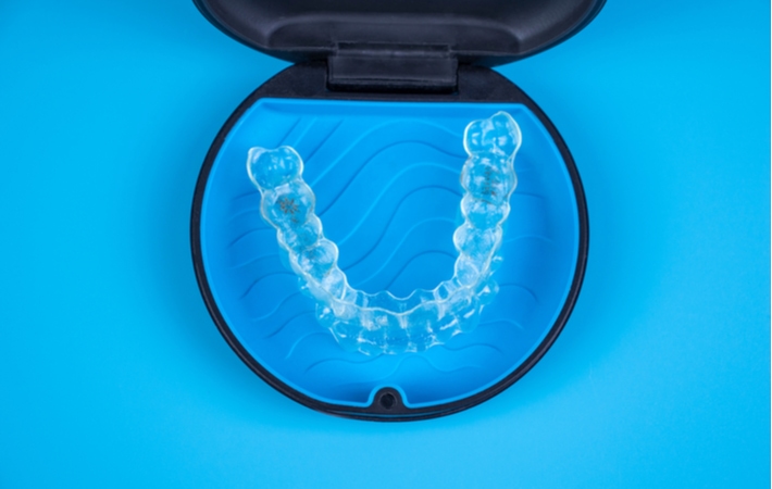 An Invisalign in its holding case resting on a bright blue background