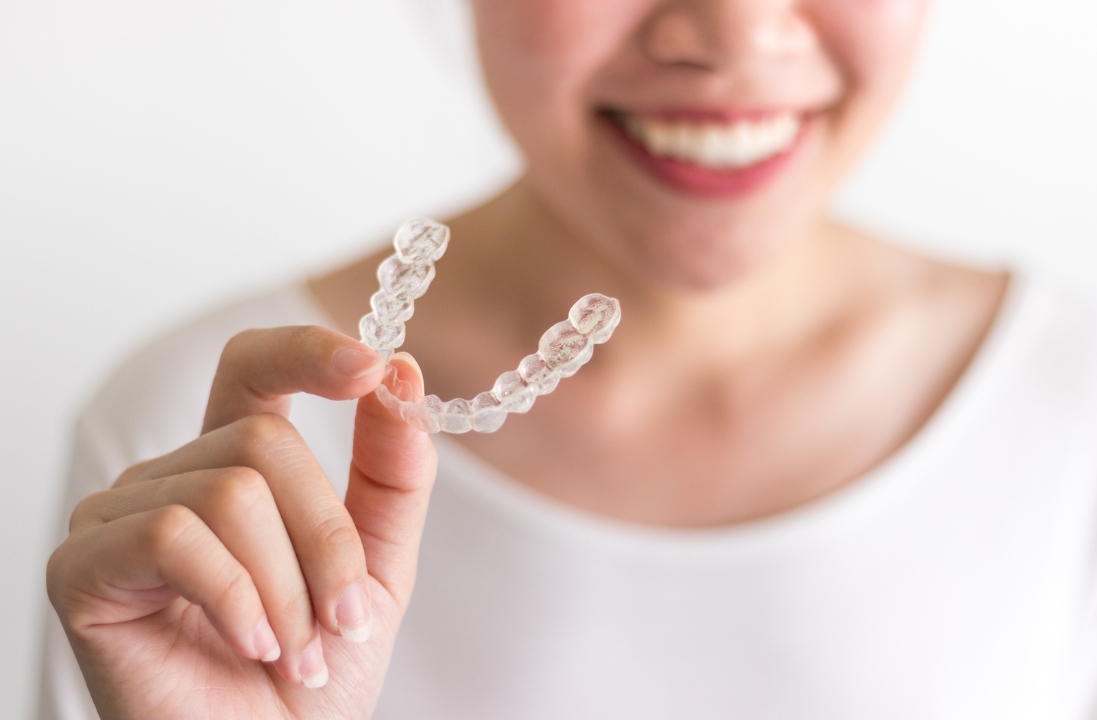 A woman smiling, blurred in the background holding an Invisalign that is in focus