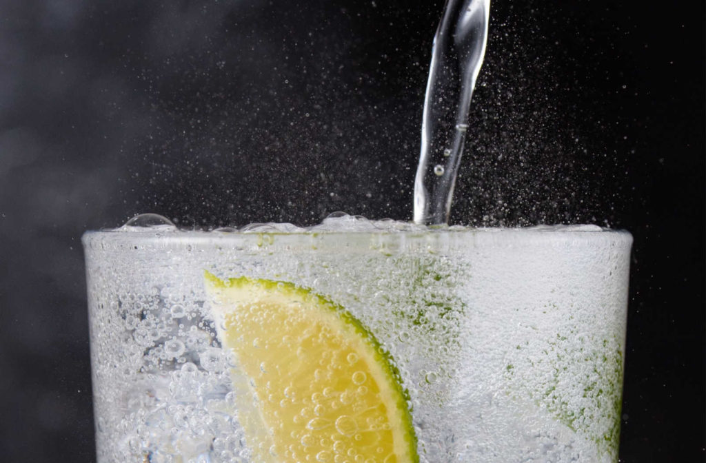 A close up of soda water being poured into a glass with a lime wedge in it.