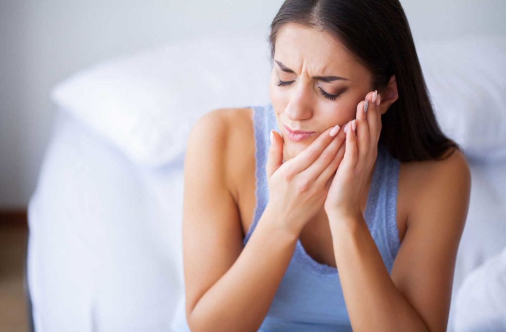 A woman holding the side of her mouth in pain because she has a toothache