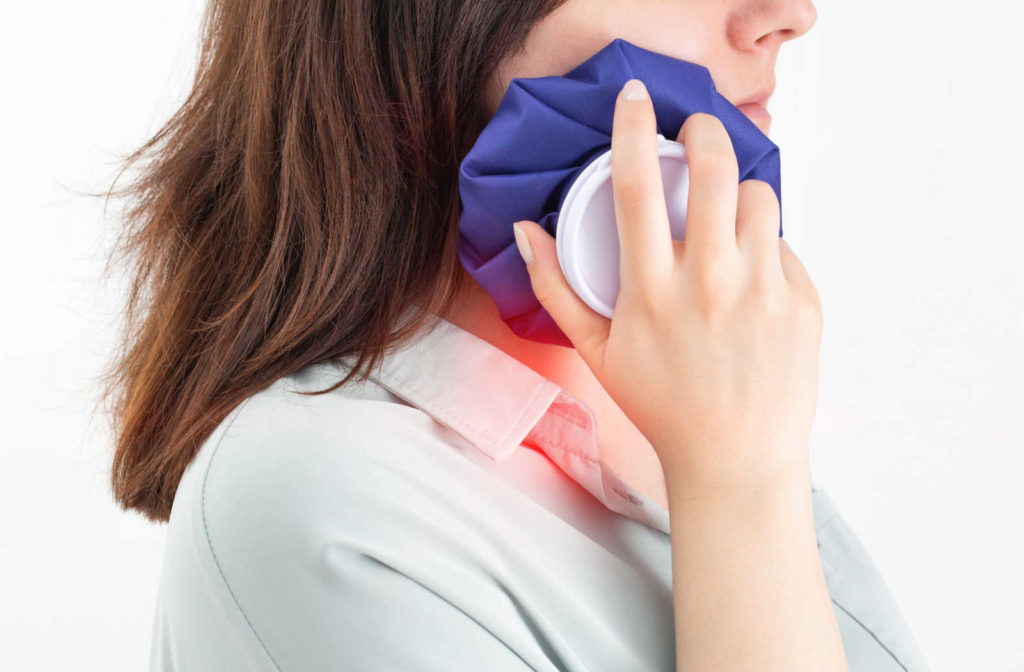 A woman holds a cold compress to her jaw to help reduce TMJ pain caused by TMD