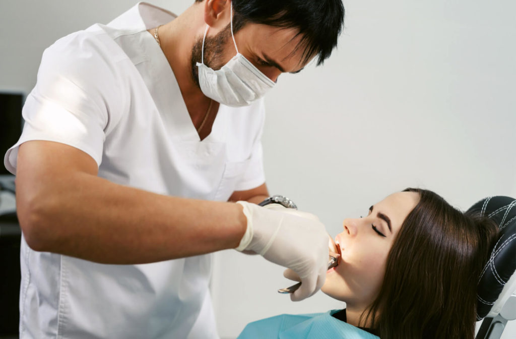 A male doctor performs a tooth extraction procedure with forceps to remove a female patient's tooth.