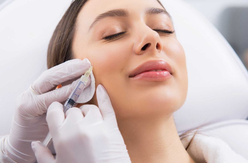 A dentist wearing sterile gloves while injecting Botox into the cheek of a female patient.