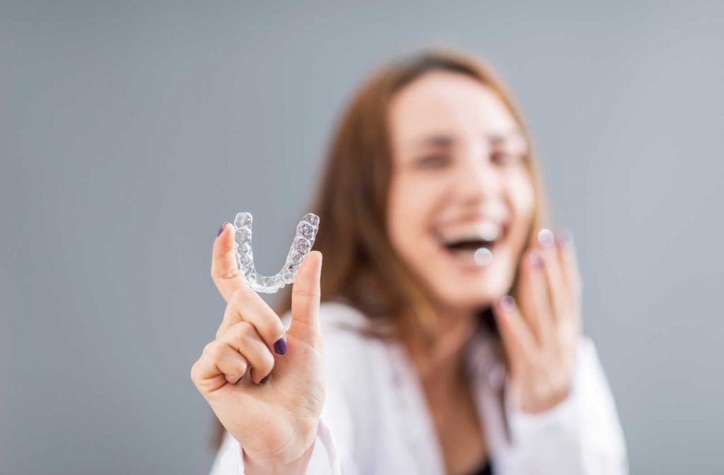 A woman holding out her Invisalign clear aligner while she's blurred in the background
