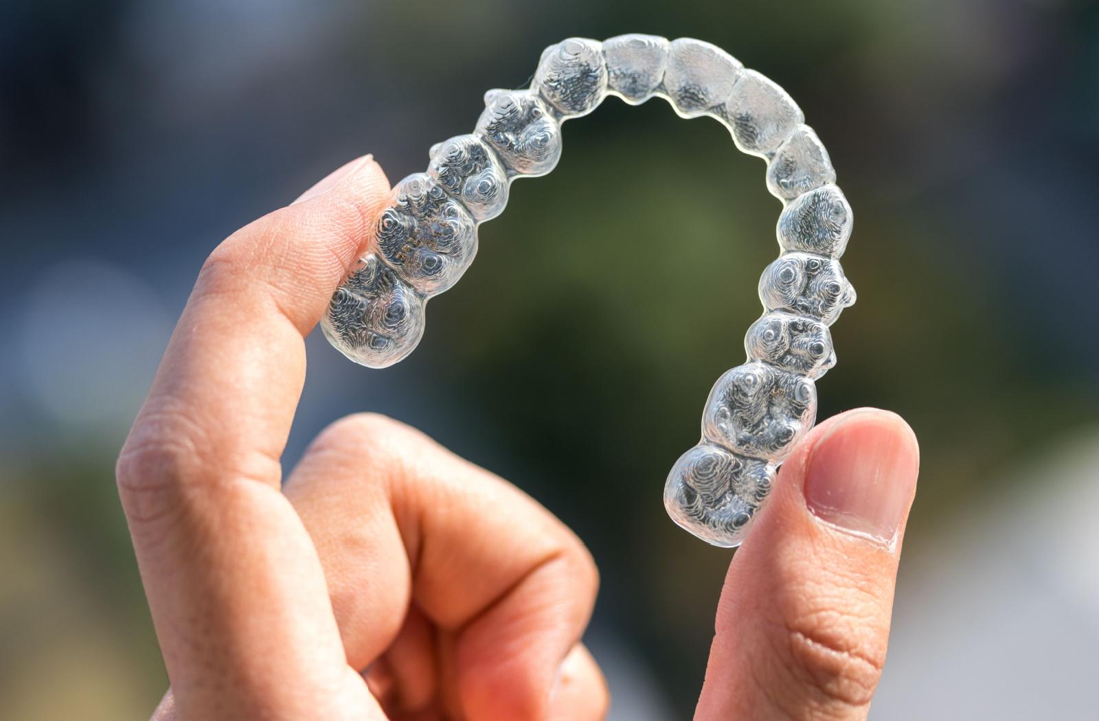 A close-up of an Invisalign being held up by two fingers.