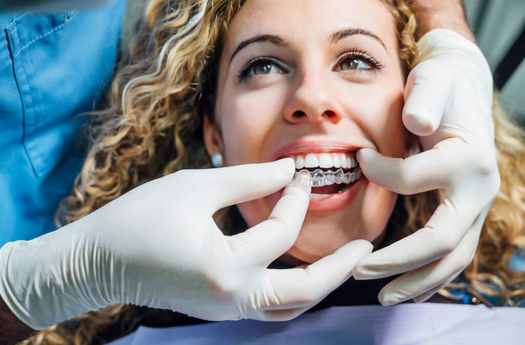 A dentist, wearing a latex gloves, puts on an Invisalign on her patient's teeth.