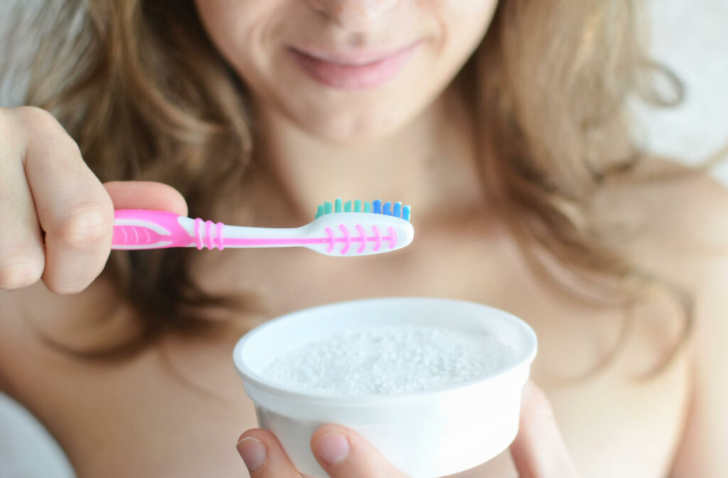 A woman using baking soda on her toothbrush to whiten her teeth.