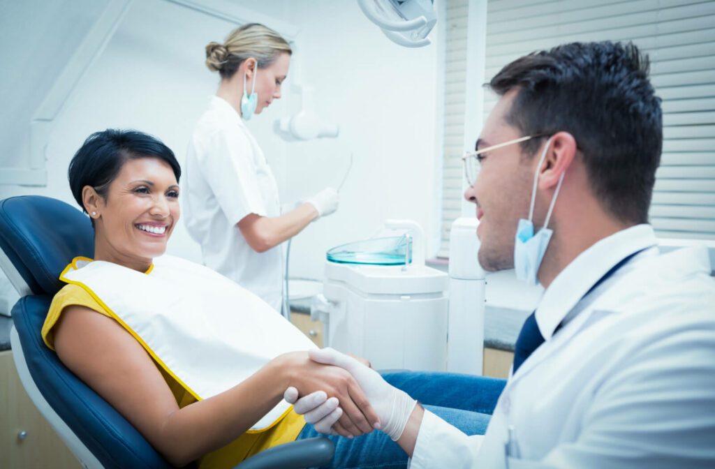 A dentist and patient shaking hands and smiling in a dental office.