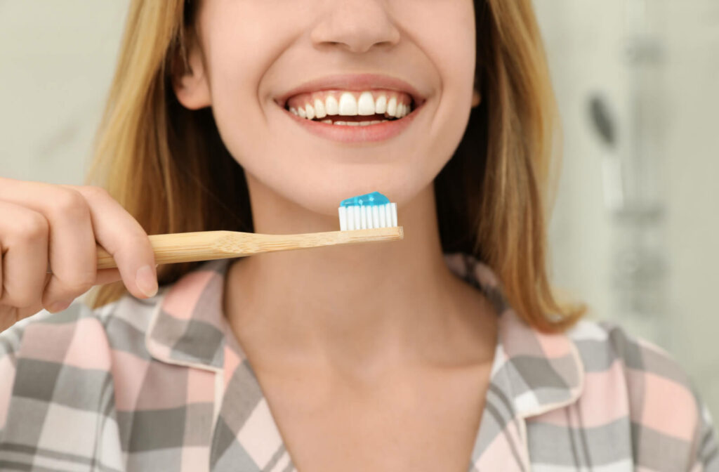 Close-up of a young woman's white smile as she holds up a toothbrush with blue toothpaste on it, about to brush.