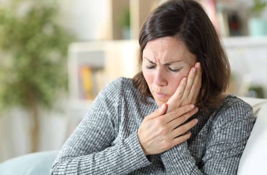 A woman in a grey sweater applying pressure to her jaw to relieve the pain caused by TMJ.