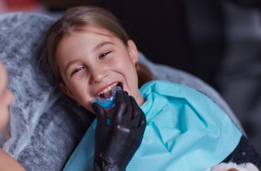 A doctor wearing a black glove carefully fitting a smiling child with a custom mouthguard.