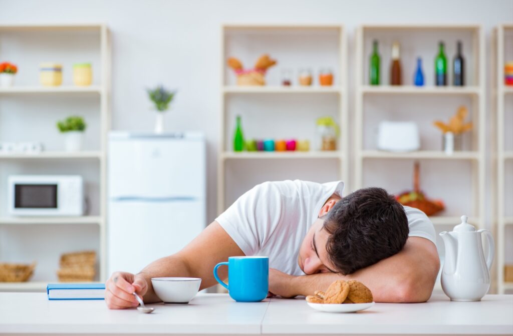 A man falling asleep on his table next to his breakfast.