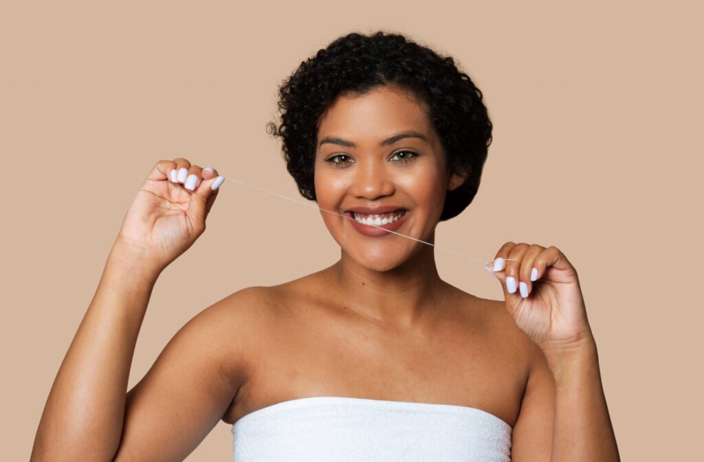 A smiling adult against a beige background holds up 18 inches of floss to demonstrate how much floss to use while flossing