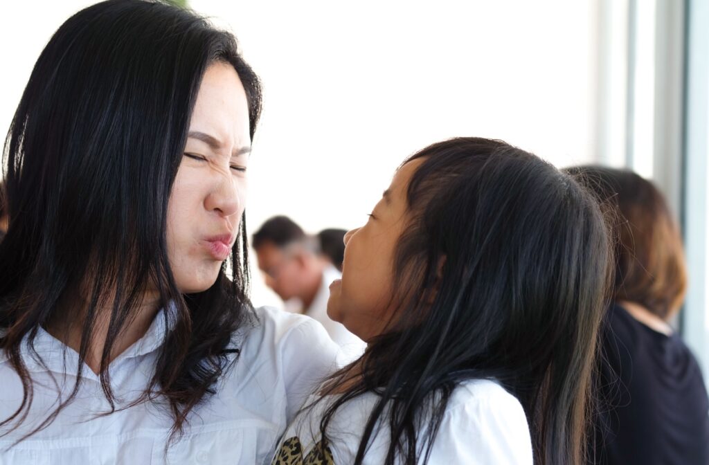 A parent holding their child winces at their bad breath as their child grins at them.