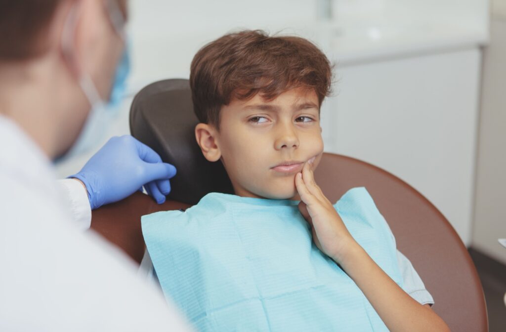 A young dental patient holds their mouth while looking suspiciously at a dental hygienist.