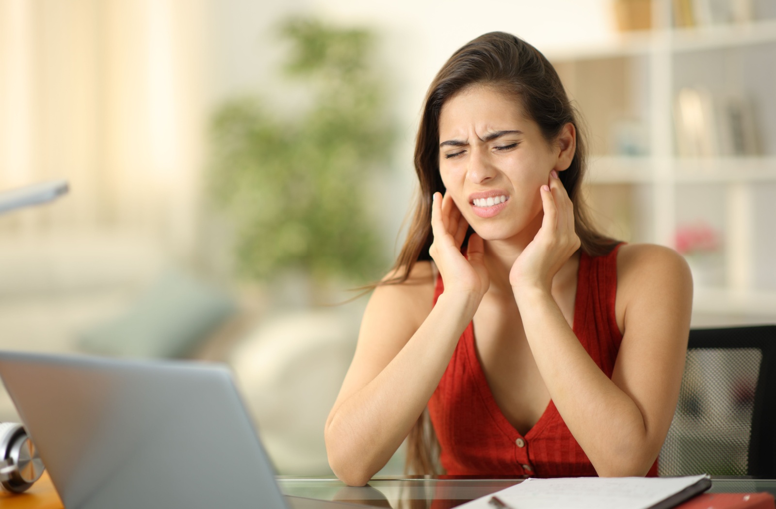 A person working at a desk rubs their sore jaw joint.