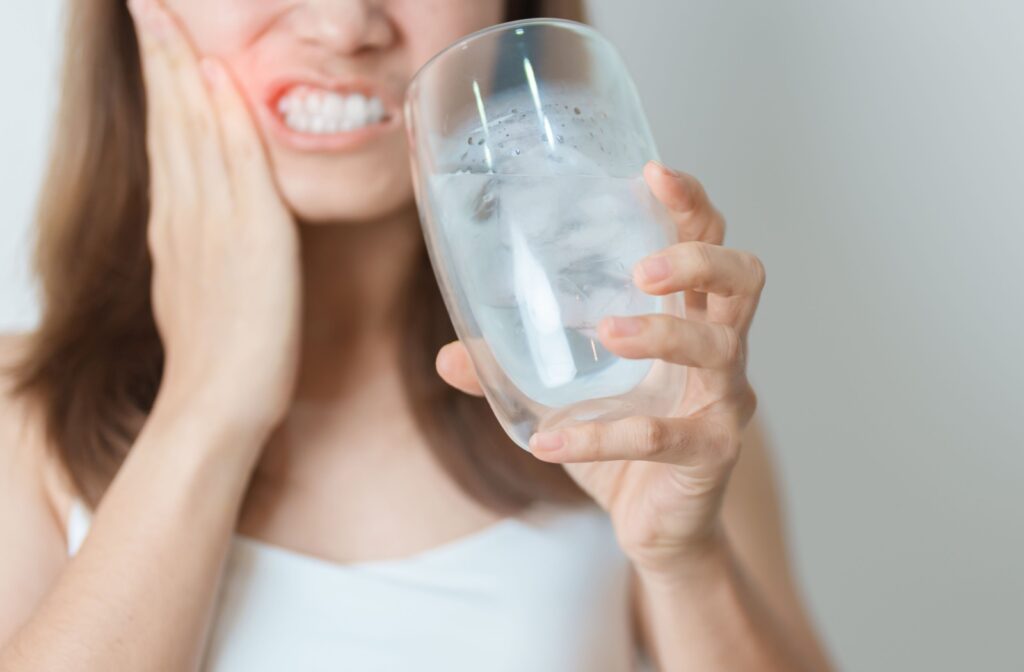 An adult rubs their jaw in pain after drinking cold water, a sign that their root canal may need more attention