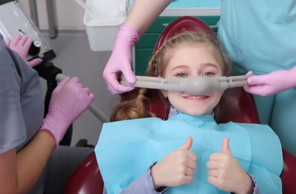 A young child smiles and gives two thumbs up as a dental hygienist sets about preparing them for sedation dentistry