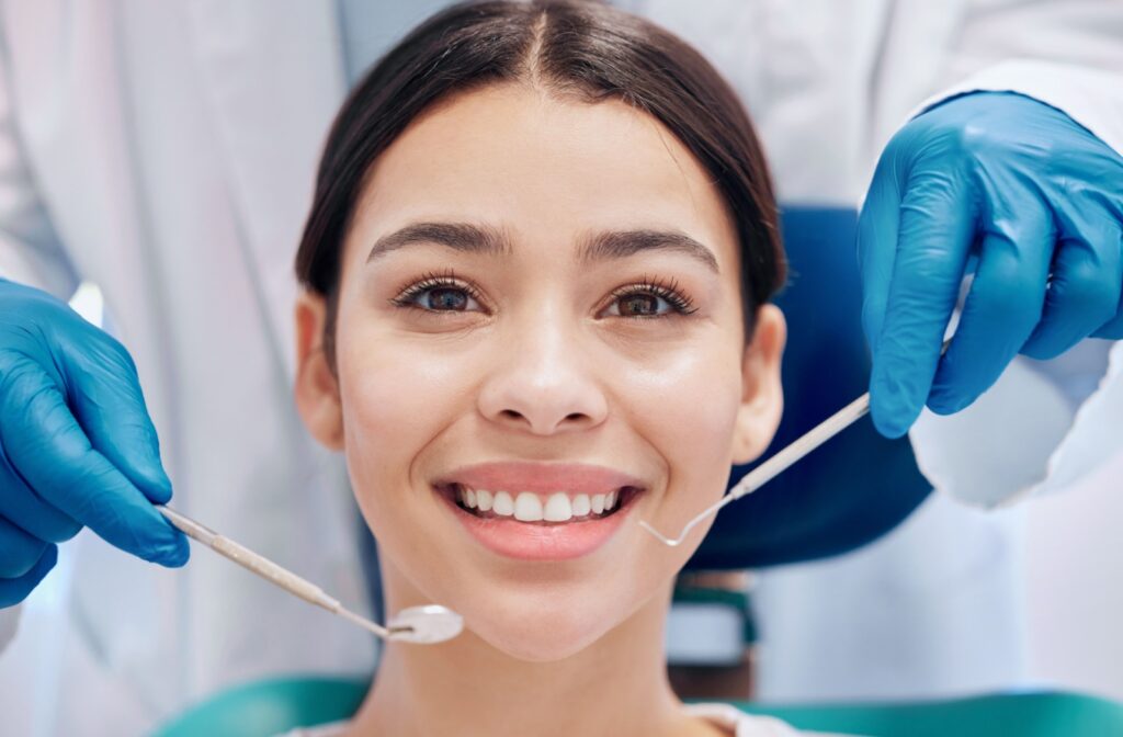 Someone smiles as a dentist holds out their cleaning tools.