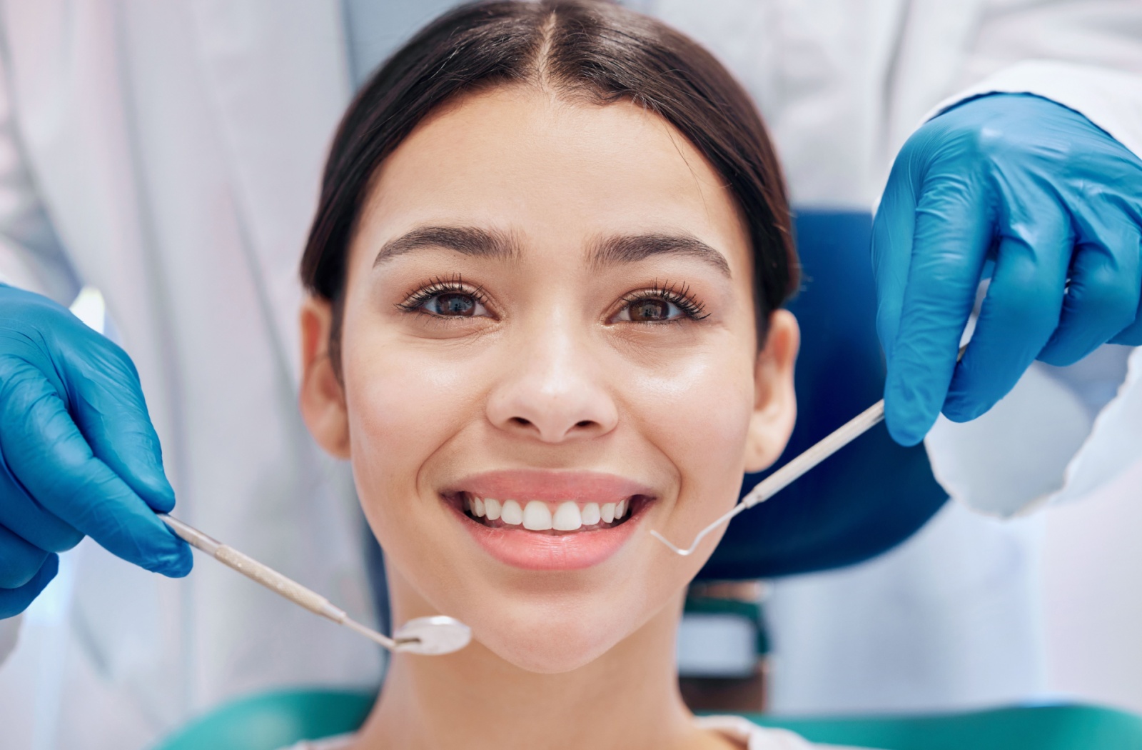 Someone smiles as a dentist holds out their cleaning tools.