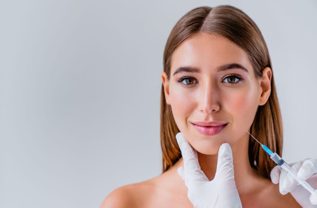 A person smiles while receiving an injection for TMJ disorder, with a gloved hand gently supporting their chin.