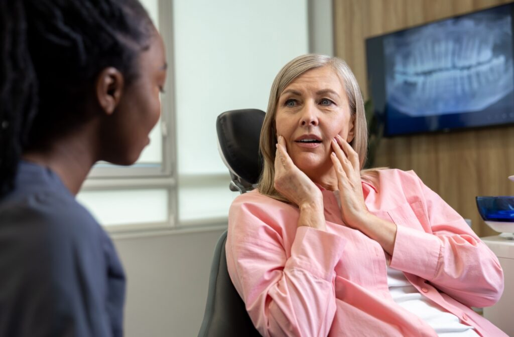 Person holding the sides of their face while discussing TMJ injections with a dentist.