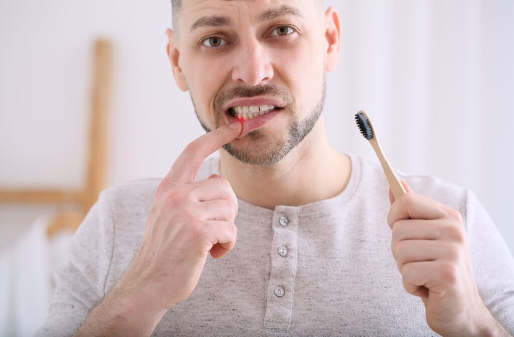 A person holds a toothbrush and points to their red, irritated gums while looking concerned.