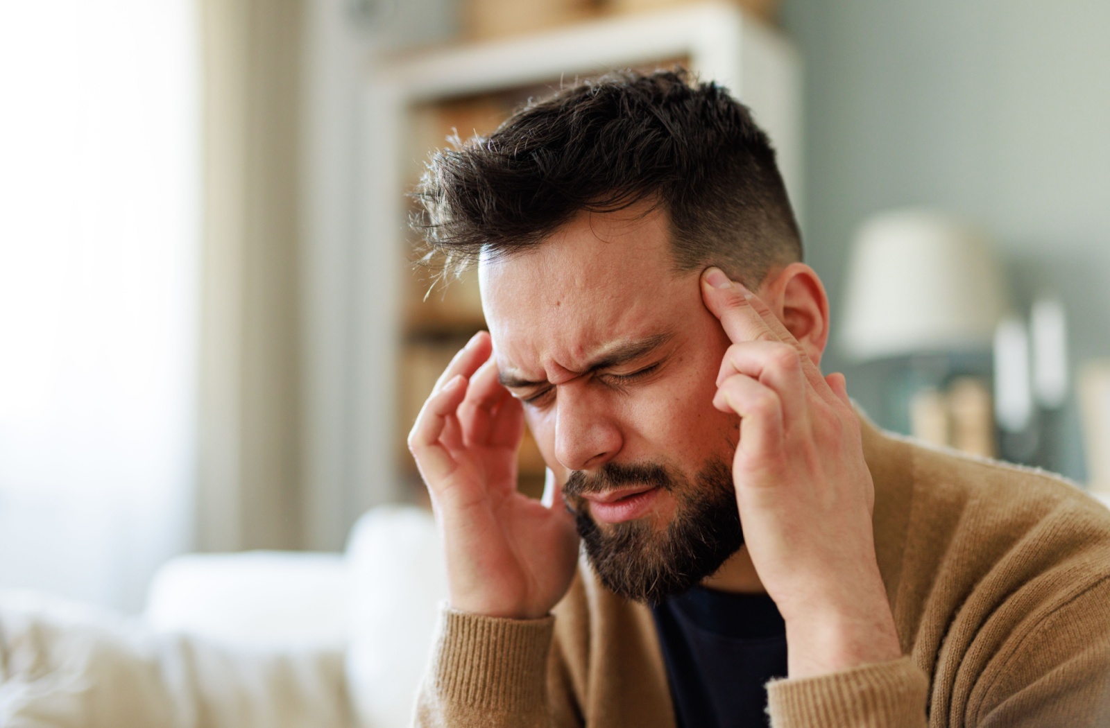 A person rubs their temples to sooth their headache while sitting on the couch