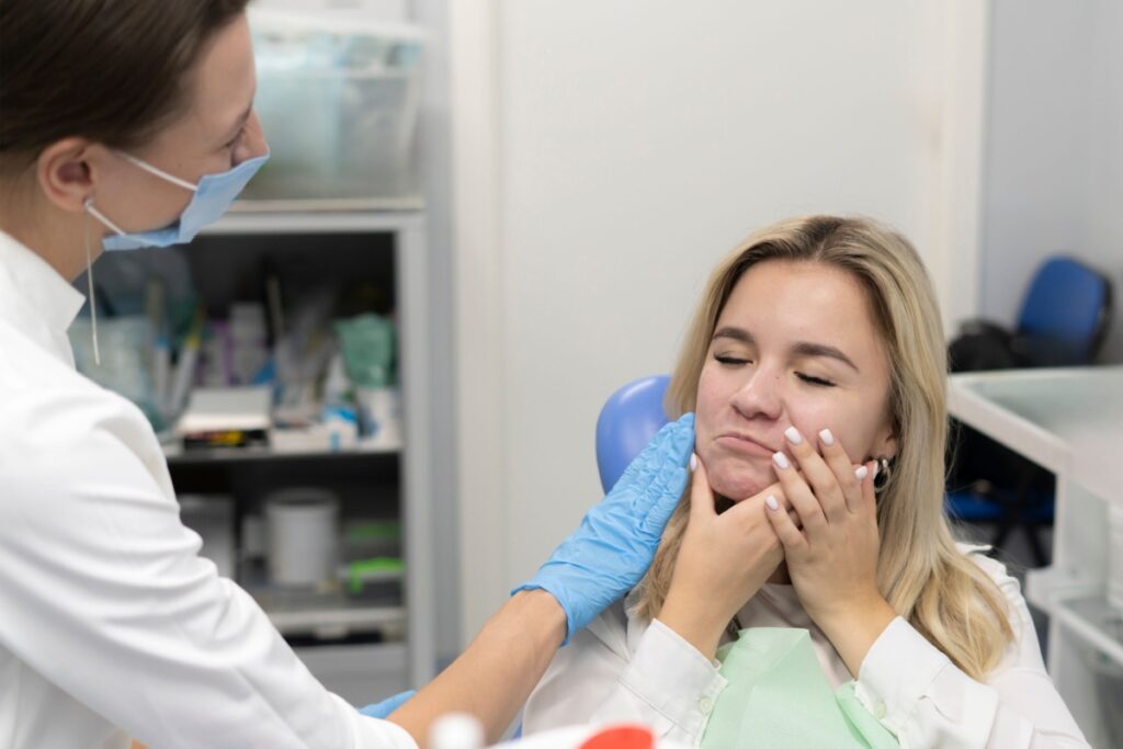 A person visiting the dentist and holding their jaw from jaw pain caused by TMJ