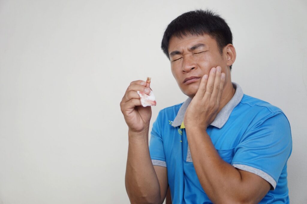 A person holding their jaw with one hand and tooth gauze in the other that was used for their tooth extraction