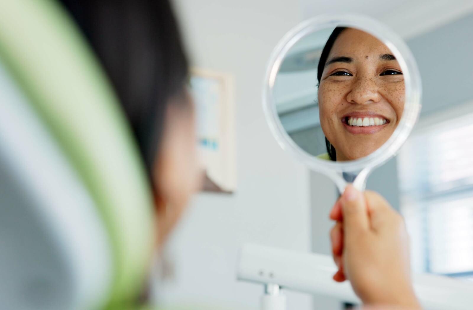 a person smiling looking at their teeth in a mirror at the dentist